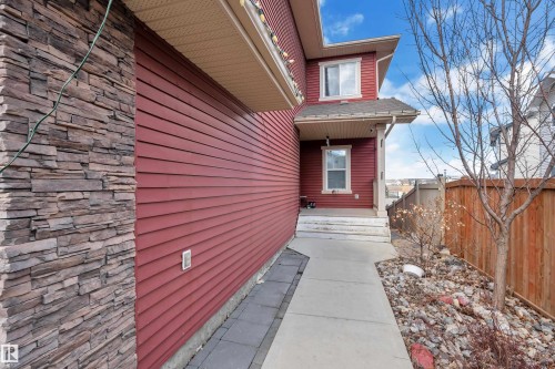 Red siding exterior with stacked stone column accent, featuring a covered entryway with white trim and a concrete walkway - 3071 Carpenter Landing Sw, Edmonton, AB 