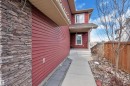 Red siding exterior with stacked stone column accent, featuring a covered entryway with white trim and a concrete walkway - 3071 Carpenter Landing Sw, Edmonton, AB 