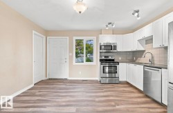 Kitchen featuring white cabinetry, stainless steel appliances, a tiled backsplash, and wood-finish flooring - 