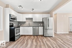 Kitchen featuring white cabinetry, stainless steel appliances, grey subway tile backsplash, dark countertops, and wood-finish flooring - 