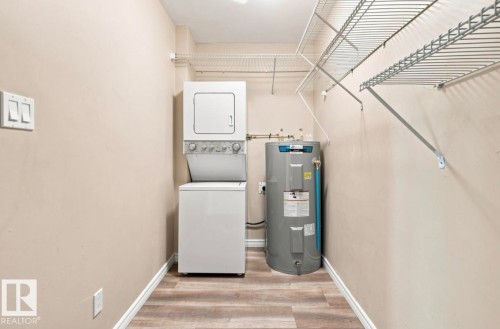 Dedicated utility area with stacked laundry appliances, water heater, wood-finish flooring, and wire shelving - 15812 110A Avenue Nw, Edmonton, AB 