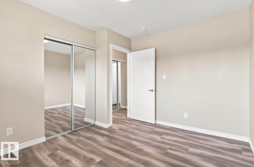 Wood-finish flooring, neutral wall tones, mirrored closet doors, and white trim - 15812 110A Avenue Nw, Edmonton, AB 