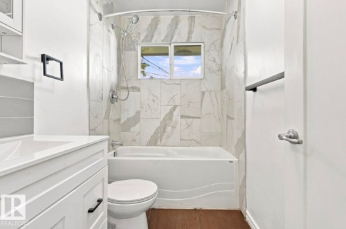 White paneled vanity with an integrated sink, shower-over-tub combination with marble-look tile surround, and wood-finish flooring - 15812 110A Avenue Nw, Edmonton, AB 