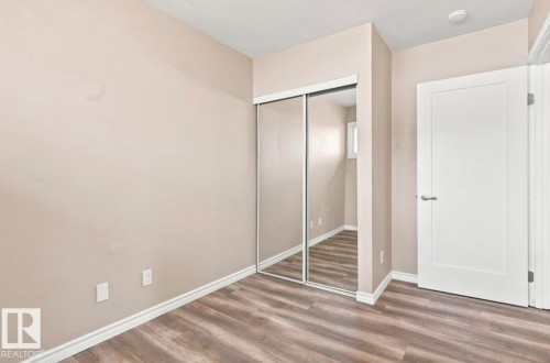 Wood-finish flooring, mirrored closet doors, and a white panel door with modern hardware - 15812 110A Avenue Nw, Edmonton, AB 