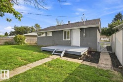 Expansive backyard featuring a concrete patio, wooden deck with stairs, white exterior door, and fenced perimeter - 