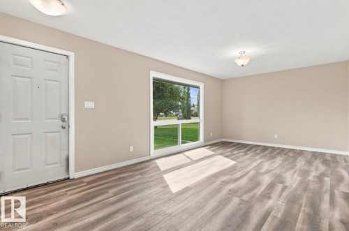 Spacious room featuring wood-finish flooring, a large picture window, and neutral wall tones - 15812 110A Avenue Nw, Edmonton, AB 