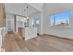 Open-concept kitchen and dining area featuring wood-finish flooring, a kitchen island with a waterfall countertop, pendant lighting, and abundant natural light from large windows - 