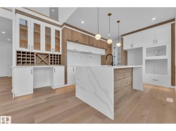 Kitchen featuring wood-finish flooring, two-tone cabinetry with glass inserts, a built-in wine rack, a waterfall island, and pendant lighting - 