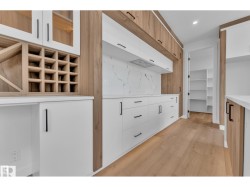 White cabinetry with matte black hardware, wood-finish flooring, white countertops, built-in wine storage, and a pantry with shelving - 