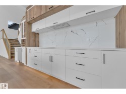 White cabinetry with black hardware, wood-finish flooring, white countertop, white backsplash with gray veining, and integrated range hood - 