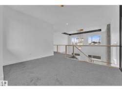 Carpeted open loft area featuring a glass railing, recessed lighting, and a prominent chandelier - 