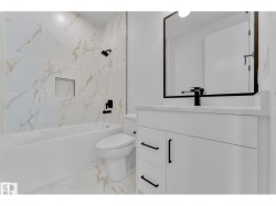 White tile flooring extending to the shower surround, white bathtub with a built-in niche, white vanity with black hardware, and a black-framed mirror - 