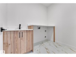 Wood-finish cabinetry with black hardware, white countertop with integrated sink, black wall-mounted faucet, and marble-look tile flooring - 