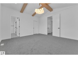 Vaulted ceiling with exposed wood beams, contemporary chandelier, gray carpet, and white doors with matte black hardware - 