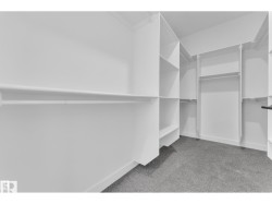 Walk-in wardrobe featuring extensive built-in shelving, multiple hanging rods, and gray carpet flooring - 