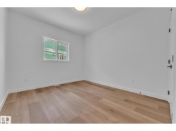 Wood-finish flooring, white painted walls, and a single window with white trim - 