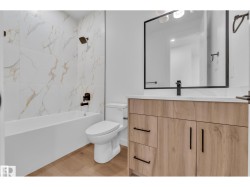 Wood-finish flooring, white vanity with black hardware, white countertop, and a black-framed mirror - 