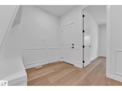 Wood-finish flooring, white paneled wainscoting, white doors with black hardware, and recessed lighting - 
