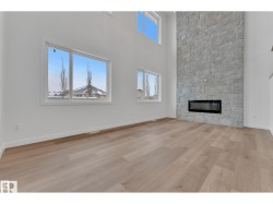 Vaulted ceiling with upper windows, stone-finish fireplace surround, built-in electric fireplace, and wood-finish flooring - 