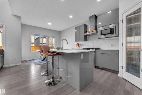 Contemporary kitchen featuring glossy grey cabinetry, an integrated stainless steel microwave, a range hood, and a gas cooktop - 2606 Donaghey Crescent Sw, Edmonton, AB - Indoor Photo Showing Kitchen With Upgraded Kitchen