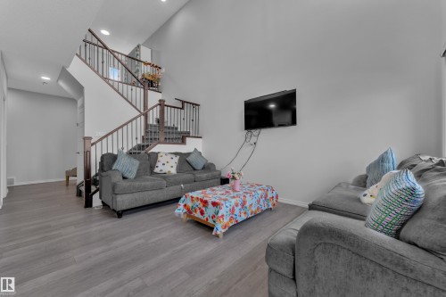 Living area featuring wood-finish flooring, a two-story ceiling, a staircase with dark wood handrails and metal balusters, and recessed lighting - 2606 Donaghey Crescent Sw, Edmonton, AB - Indoor Photo Showing Living Room