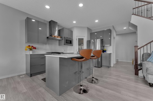 Contemporary kitchen featuring gray high-gloss cabinetry, white countertops, a stainless steel range hood, and light wood-finish flooring - 2606 Donaghey Crescent Sw, Edmonton, AB - Indoor Photo Showing Kitchen With Upgraded Kitchen