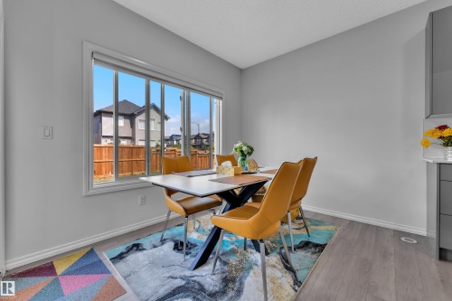 Bright dining area featuring a large window, light gray walls, and wood-finish flooring - 2606 Donaghey Crescent Sw, Edmonton, AB - Indoor