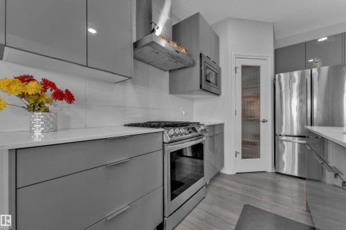 Modern kitchen featuring sleek gray cabinetry with integrated hardware, stainless steel appliances including a range and refrigerator, white solid surface countertops, and wood-finish flooring - 2606 Donaghey Crescent Sw, Edmonton, AB - Indoor Photo Showing Kitchen With Stainless Steel Kitchen With Upgraded Kitchen