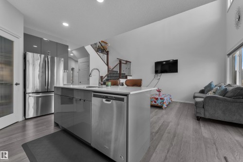 Open-concept living space featuring a kitchen island with integrated sink, stainless steel appliances, wood-finish flooring, and a two-story ceiling - 2606 Donaghey Crescent Sw, Edmonton, AB - Indoor Photo Showing Kitchen With Stainless Steel Kitchen
