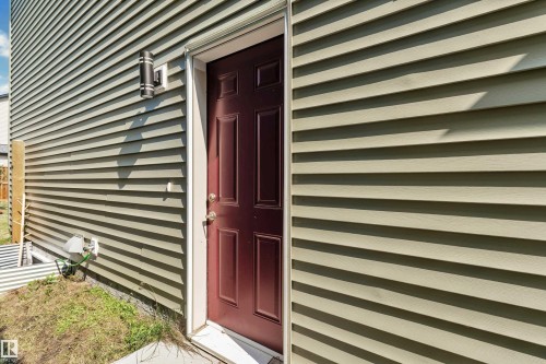 Rich burgundy paneled door with polished hardware, complemented by light green horizontal siding and a modern exterior light fixture - 2606 Donaghey Crescent Sw, Edmonton, AB -  Photo Showing Other Room