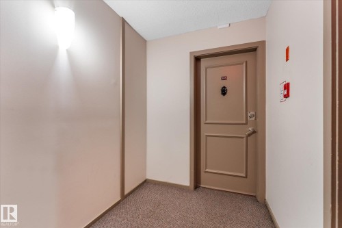 Entryway with a paneled door, wall-mounted light fixture, and carpet flooring - #205 8125 110 St Nw, Edmonton, AB 