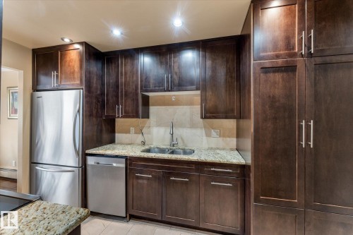 Dark wood-finish cabinetry, stainless steel appliances, speckled stone countertops, and a tile backsplash - #205 8125 110 St Nw, Edmonton, AB 