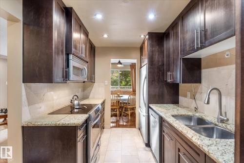 Galley kitchen featuring dark wood-finish cabinetry, light-toned countertops, tile flooring, stainless steel appliances, and recessed lighting - #205 8125 110 St Nw, Edmonton, AB 