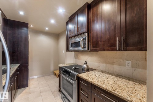 Rich wood-finish cabinetry, stainless steel appliances, speckled stone countertops, tiled backsplash, and recessed lighting - #205 8125 110 St Nw, Edmonton, AB 