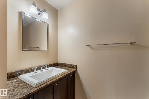 Vanity with a rectangular undermount sink, a dark veined countertop, and dark wood-finish cabinetry - #205 8125 110 St Nw, Edmonton, AB 