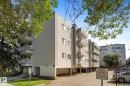 Multi-story building featuring light-colored siding, multiple balconies with white railings, and a ground-level parking area - #205 8125 110 St Nw, Edmonton, AB 
