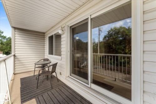 Covered balcony with white siding, white railing, and a sliding glass door - #205 8125 110 St Nw, Edmonton, AB 