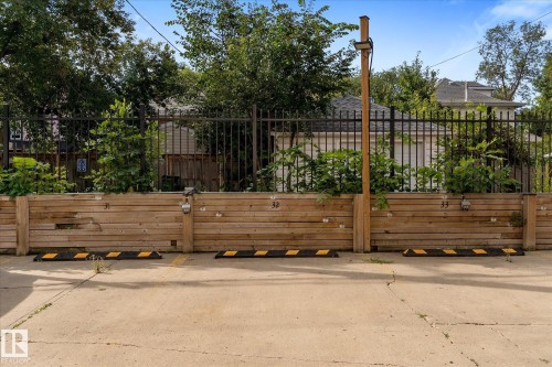 Paved parking area featuring designated spaces, timber retaining wall, and wrought iron fencing - #205 8125 110 St Nw, Edmonton, AB 