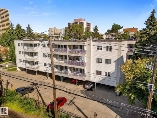 Multi-story building with white siding, multiple balconies, and an integrated carport parking area - #205 8125 110 St Nw, Edmonton, AB 
