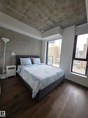 Exposed concrete ceiling, full-height windows, dark wood-finish flooring, and concrete accent wall - #1006 1010 6 St Sw, Calgary, AB 