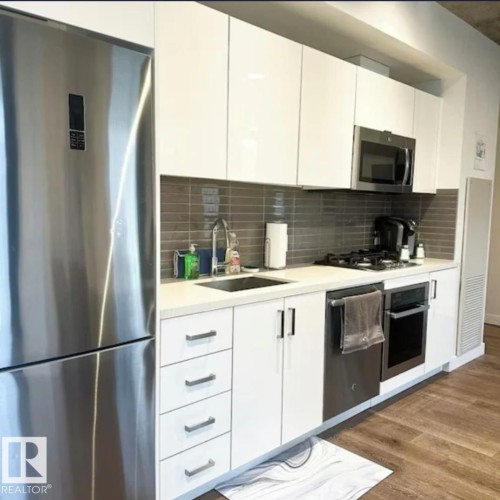 Sleek kitchen featuring stainless steel appliances, white flat-panel cabinetry, a gray subway tile backsplash, and wood-finish flooring - #1006 1010 6 St Sw, Calgary, AB 