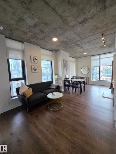 Open-concept living space featuring wood-finish flooring, exposed concrete ceiling, recessed lighting, and expansive windows with roller shades - #1006 1010 6 St Sw, Calgary, AB 