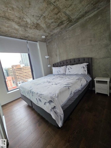 Exposed concrete ceiling and walls, large window with roller shades, and dark wood-finish flooring - #1006 1010 6 St Sw, Calgary, AB 