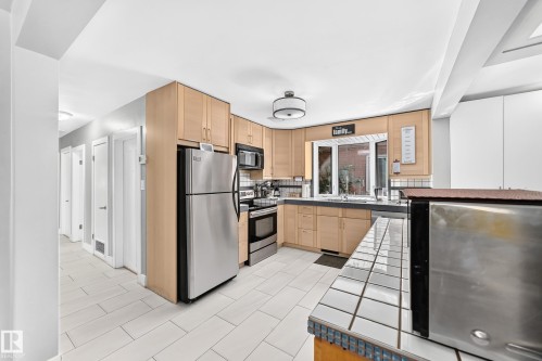 Kitchen featuring stainless steel appliances, wood-finish cabinetry, tile backsplash, and a window above the sink - 10139 74 Street Nw, Edmonton, AB 