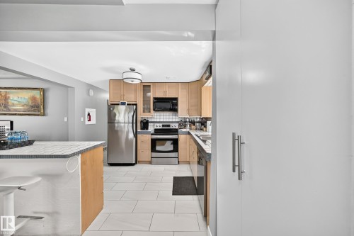 Kitchen featuring light wood cabinetry, stainless steel appliances, a tile backsplash, and light-toned floor tiling - 10139 74 Street Nw, Edmonton, AB 