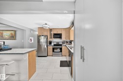 Kitchen featuring light wood cabinetry, stainless steel appliances, a tile backsplash, and light-toned floor tiling - 