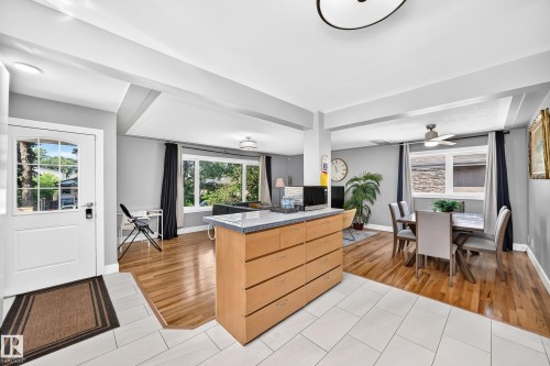 Open-concept living space with light wood-finish flooring, white tile entry, and a kitchen island featuring light wood-finish cabinetry and a light-toned countertop - 10139 74 Street Nw, Edmonton, AB 