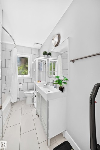 White subway tile shower surround, rectangular vanity mirror, single basin vanity with integrated sink, white tile flooring, and a window with privacy glass - 10139 74 Street Nw, Edmonton, AB 