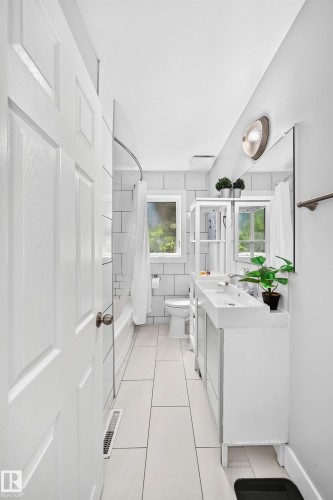 White subway tile shower surround, rectangular white floor tiles, dual basin vanity, white toilet, and a window providing natural light - 10139 74 Street Nw, Edmonton, AB 