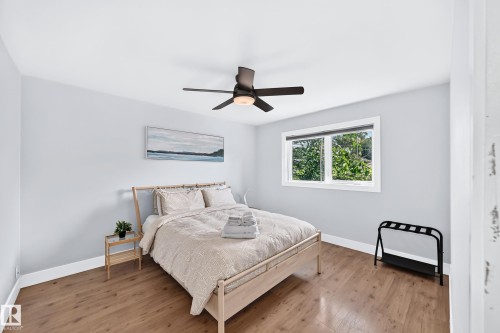 Bright room with wood-finish flooring, a contemporary ceiling fan, and a large window - 10139 74 Street Nw, Edmonton, AB 